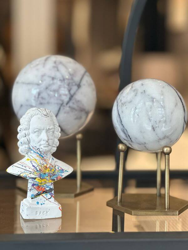 White marble decorative sphere with lilac veins on hexagonal stand, antique brass finish, alongside decorative bust.