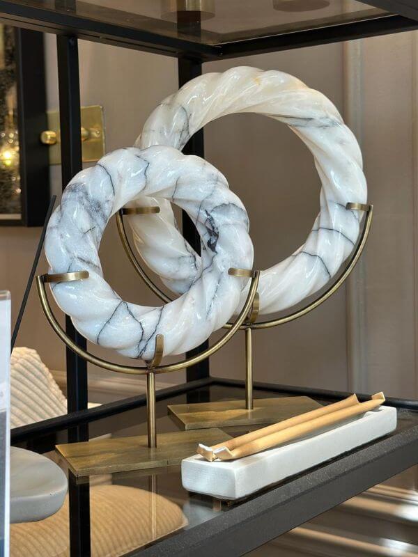 White marble twisted disk decor featuring elegant grey veining on antique brass stand, creating a sophisticated display.