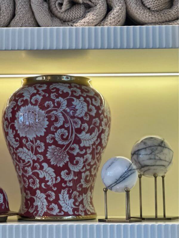 White marble decorative sphere with lilac veins displayed beside a decorative red vase on a shelf.