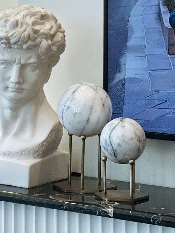 White marble decorative sphere with lilac veins on a hexagonal stand in antique brass finish.