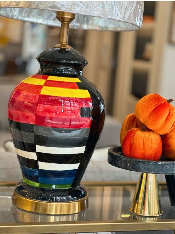 Multicolor ceramic table lamp on a table with decorative pumpkins, featuring a vibrant oval-shaped base.