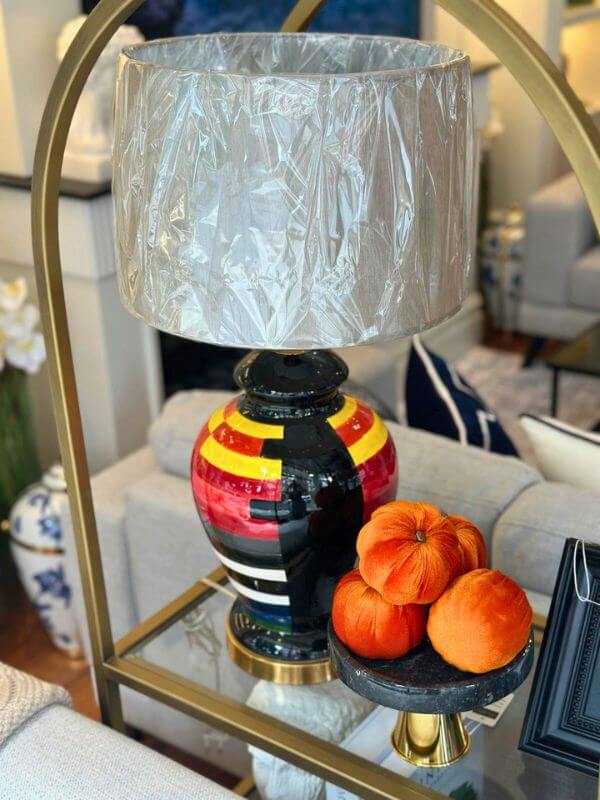 Multicolor ceramic table lamp on a table with an oval base and an artistic lamp shade, alongside orange decorative items.