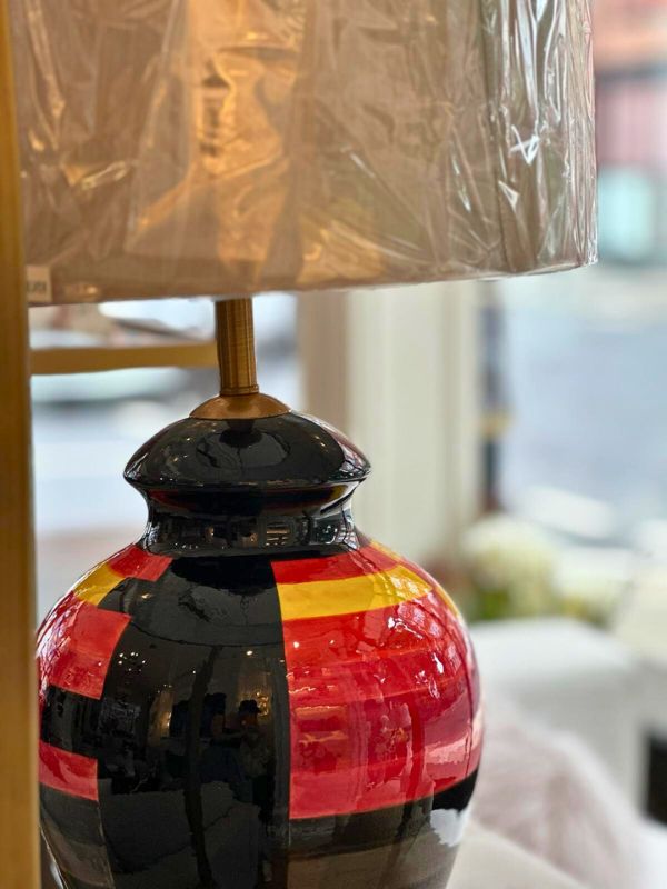 Close-up of multicolor ceramic table lamp showcasing bold red, yellow, and black patterns on the oval base.