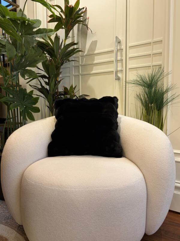cozy black faux fur throw pillow cover on a modern cream-colored chair surrounded by indoor plants