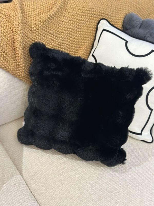 Black faux fur throw pillow cover on a sofa, showcasing its plush texture and luxurious design.