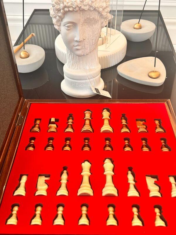 Large classic chess set pieces displayed on a red felt background with a marble bust in the background.