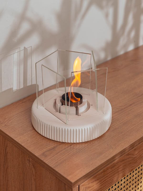 Modern concrete fireplace accent featuring glass panels and flame on a wooden surface.