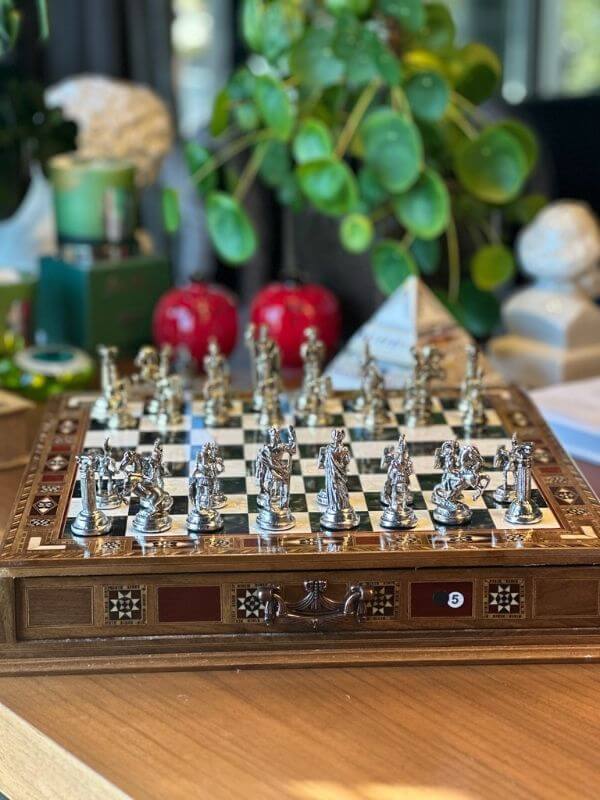 Large handmade chess set displayed with intricately designed metal pieces on a beautifully finished wooden board.