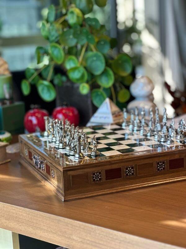Large handmade chess set displayed elegantly with intricate metal pieces and a polished wooden board.